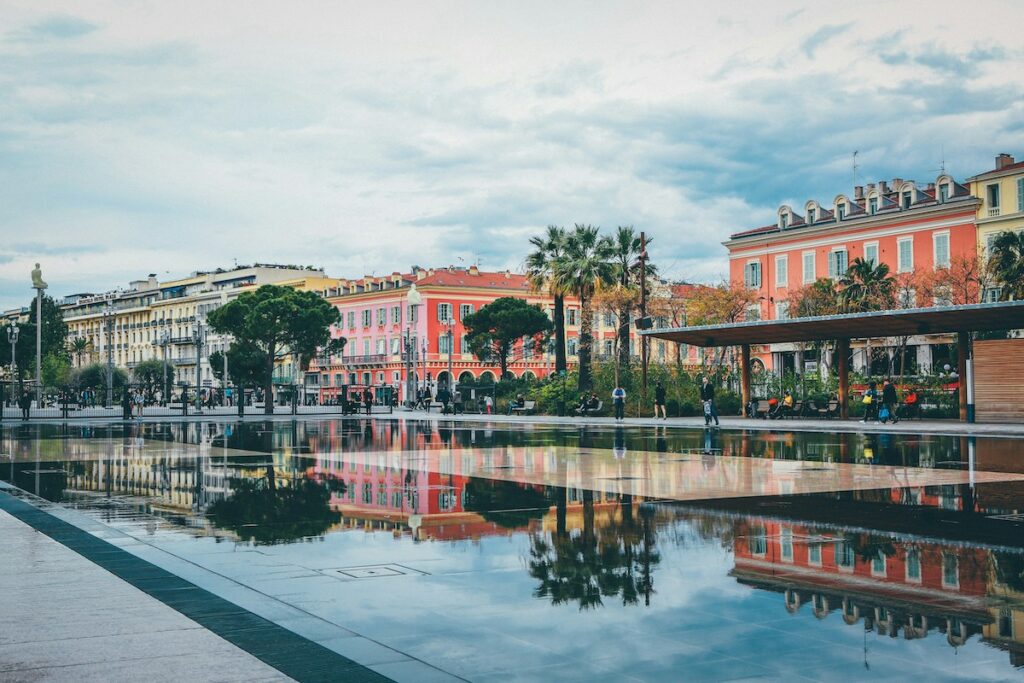 Colorful row of pastel buildings along a plaza with palm trees and a reflective pool in the foreground.