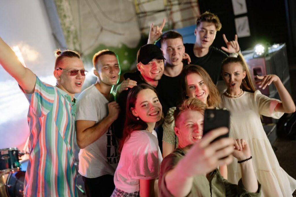 A group of friends posing for a selfie at a party, smiling and making fun gestures toward the camera