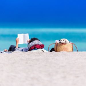 Livres vacances : Une personne qui lit allongée sur le sable - Départ 18:25