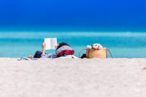 Livres vacances : Une personne qui lit allongée sur le sable - Départ 18:25