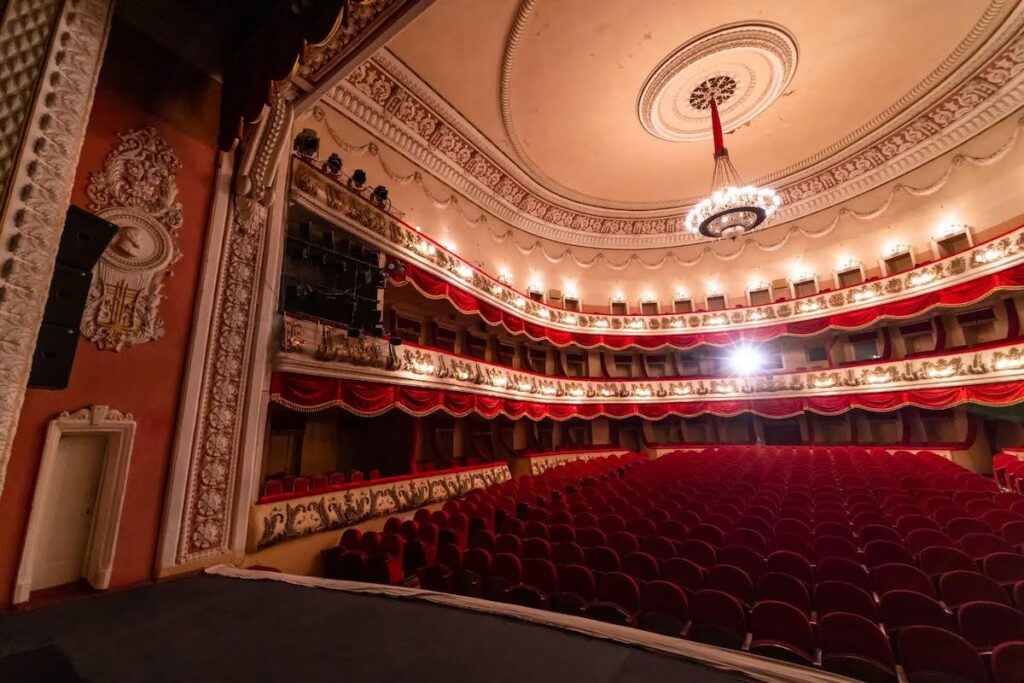 Elegant 19th-century theater interior with red upholstered seats and gilded balconies.