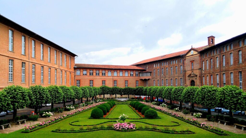 Brick university courtyard with manicured lawn, trimmed hedges, and rose beds framed by red brick buildings on both sides
