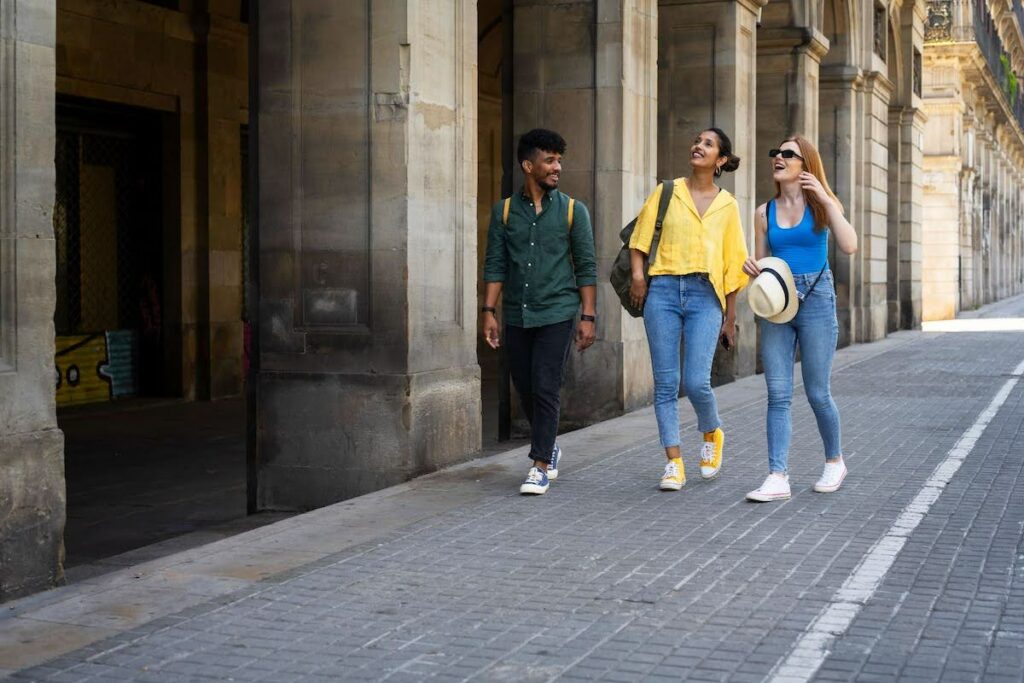 Three friends walk along a stone-arched city street, smiling and chatting as they stroll.